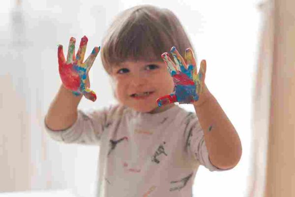 Smiling child holding up both hands covered in colorful paint